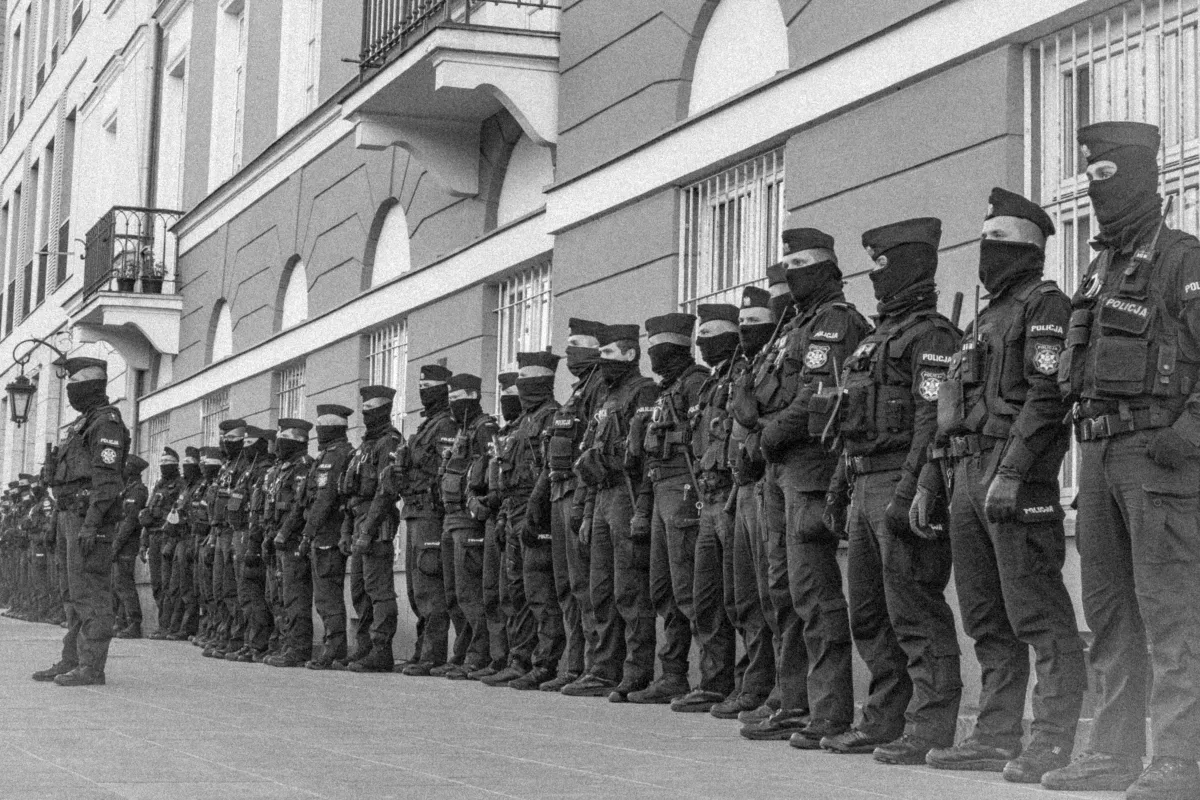 Line of masked police officers armed with long guns standing along a city street